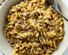Ingredients: 1 lb ground beef 1 medium onion, chopped 2 cloves garlic, minced 8 oz egg noodles 1 can (10.5 oz) cream of mushroom soup 1 can (10.5 oz) beef broth 1 cup sour cream 1 tablespoon Worcestershire sauce 1 teaspoon dried parsley Salt and pepper to taste 1 tablespoon olive oil Optional: chopped fresh parsley for garnish Instructions: Cook the Egg Noodles: Bring a large pot of salted water to a boil. Add the egg noodles and cook according to the package instructions until al dente. Drain and set aside. Cook the Beef: In a large skillet, heat the olive oil over medium heat. Add the chopped onion and cook until softened, about 3-4 minutes. Add the ground beef to the skillet. Cook, breaking it up with a spoon, until browned and no longer pink. Drain any excess fat. Add the minced garlic to the beef and cook for another minute until fragrant. Prepare the Sauce: Stir in the cream of mushroom soup, beef broth, Worcestershire sauce, dried parsley, salt, and pepper. Mix well to combine. Bring the mixture to a simmer and cook for 5-7 minutes, allowing the flavors to meld together. Combine Noodles and Sauce: Reduce the heat to low and stir in the cooked egg noodles until well coated with the sauce. Add the sour cream and gently mix until the sauce is creamy and the noodles are well coated. Serve: Taste and adjust the seasoning with more salt and pepper if needed. Serve hot, garnished with chopped fresh parsley if desired. This Easy Beef and Noodles recipe is perfect for a quick and comforting meal. Enjoy!